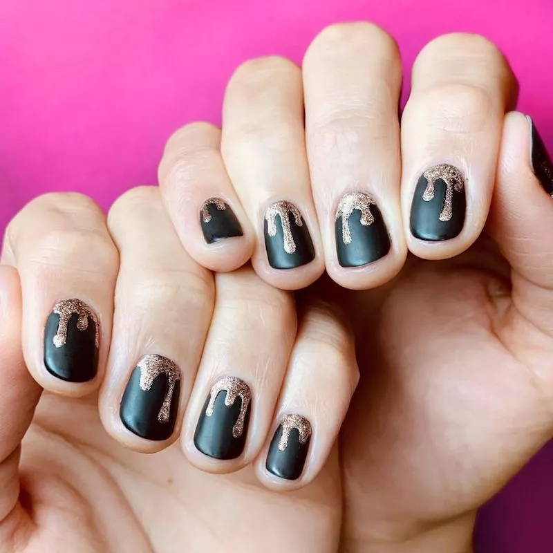 Matte black nails with sparkling gold polish dripping from cuticles