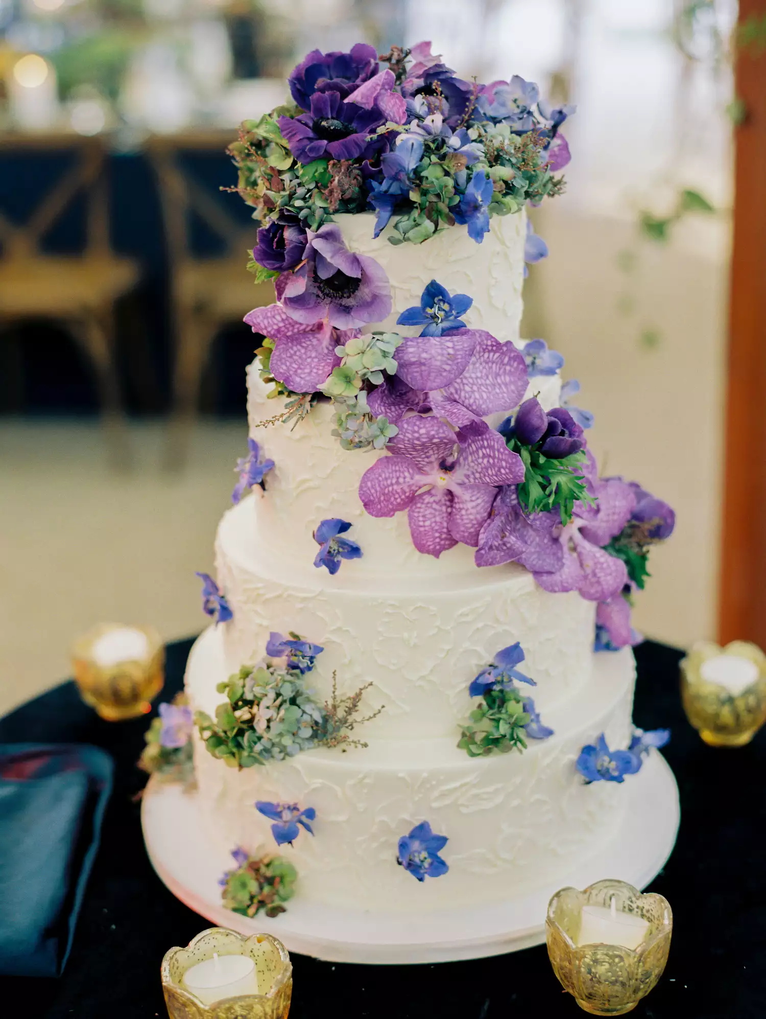 Five-tiered white wedding cake with piped flowers and fresh purple flowers cascading down the side