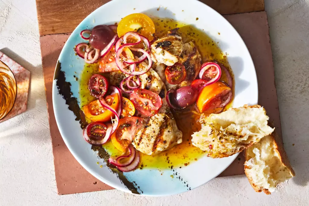 Individual plate of grilled chicken with marinated tomatoes and onions