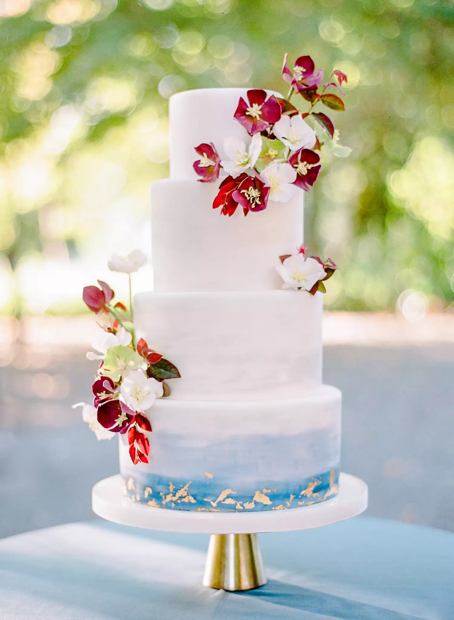 Four-Tiered White and Blue Wedding Cake with Gold Accents and Fresh Flowers