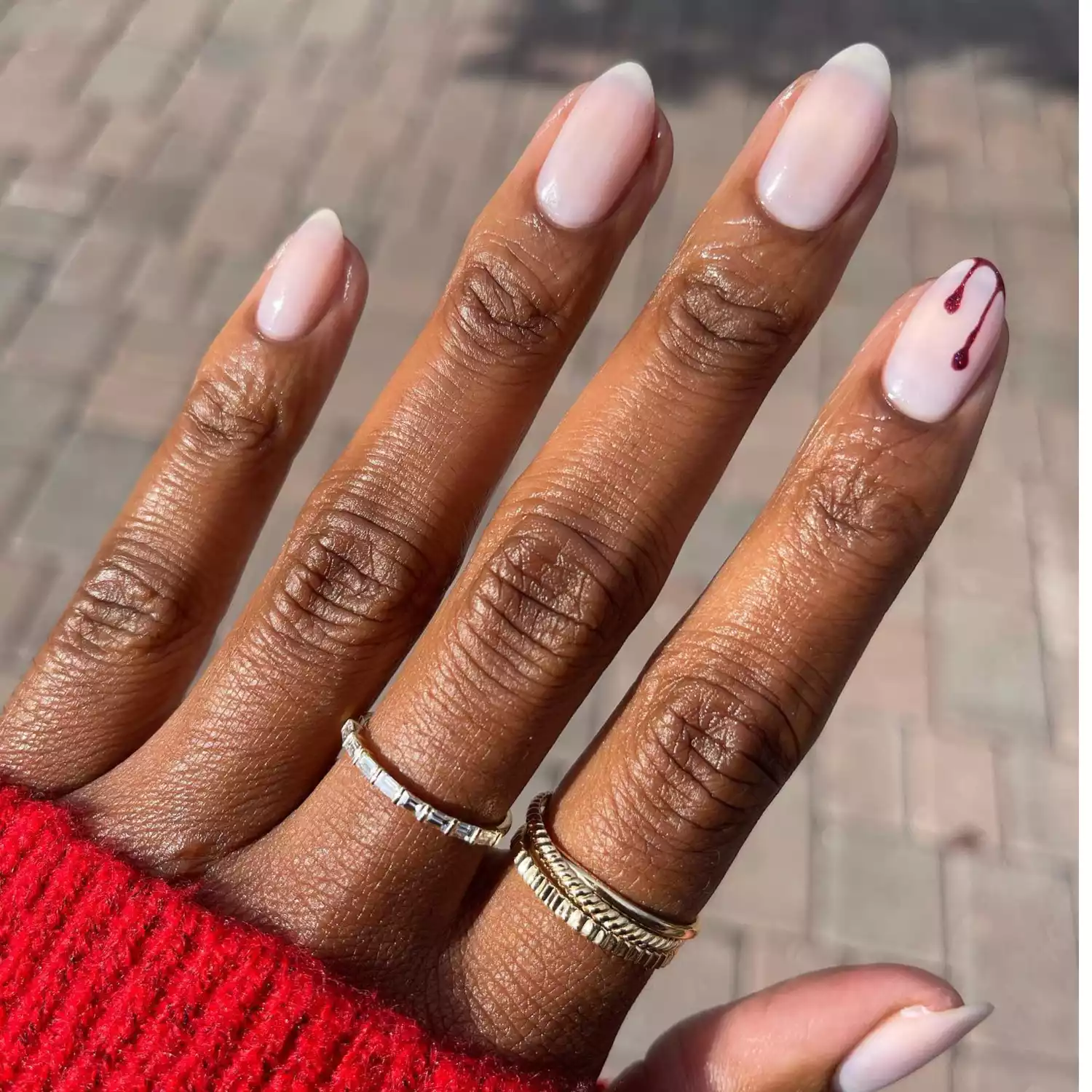 Short nails with white nail polish. One accent nail has a red blood drip. 