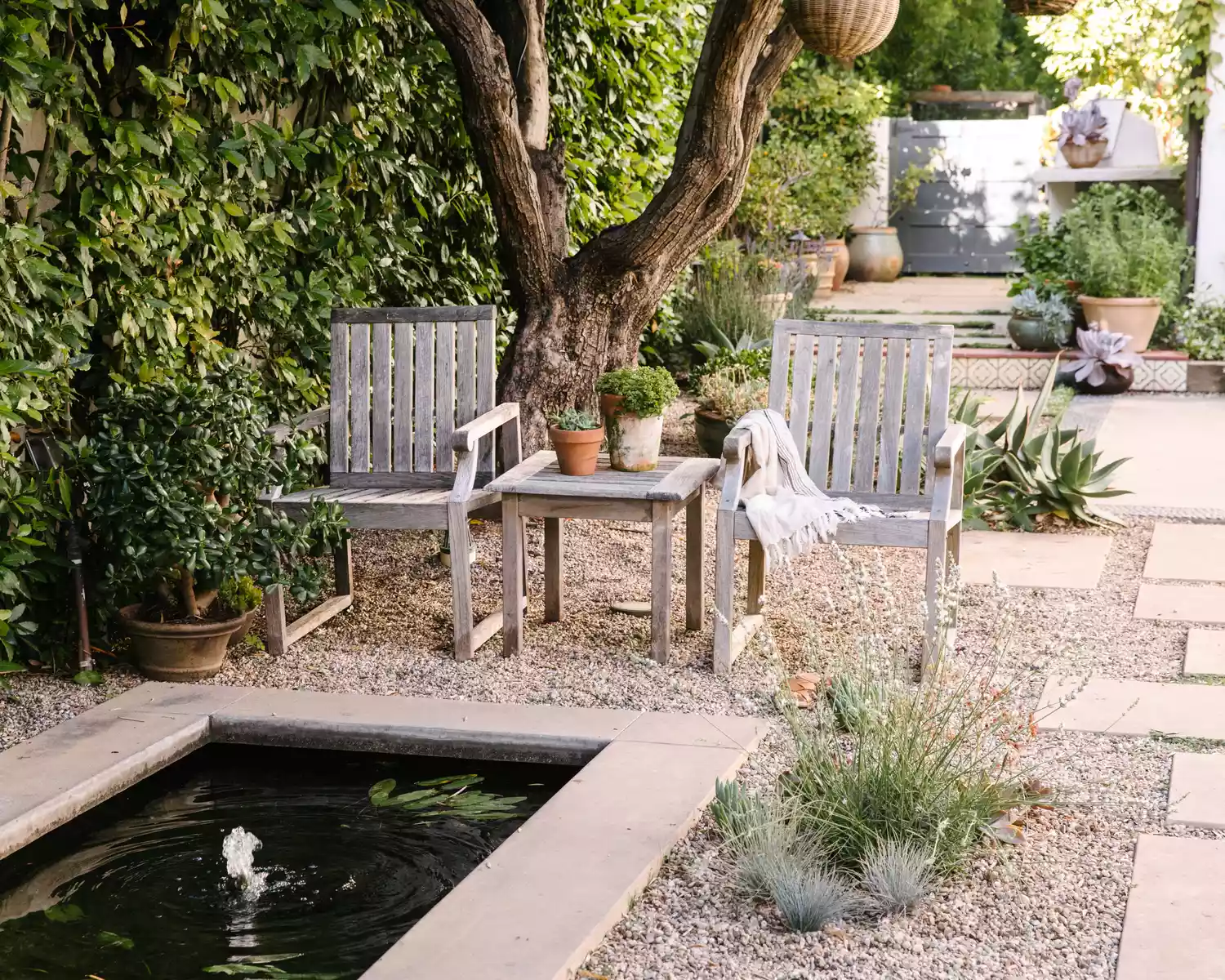 Two teak chairs next to a pond, surrounded by gravel