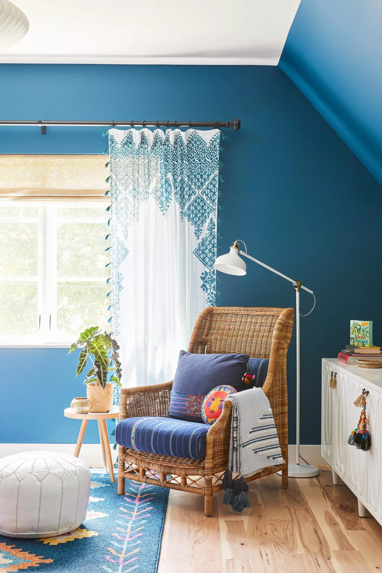 rattan chair with blue cushion in corner of blue/white bedroom