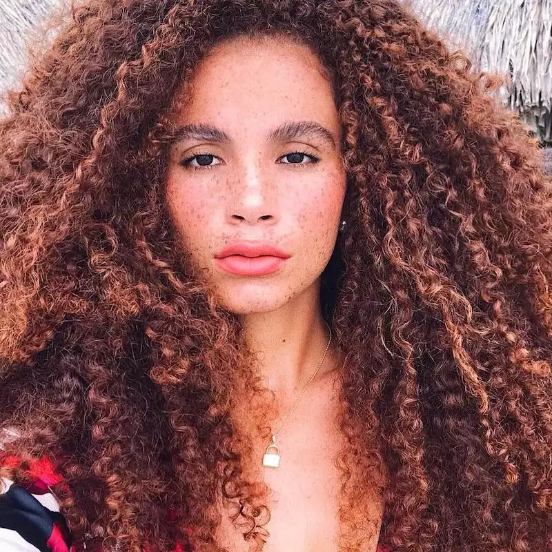 Joyjah Estrada wears her natural brunette curls with warm-toned highlights