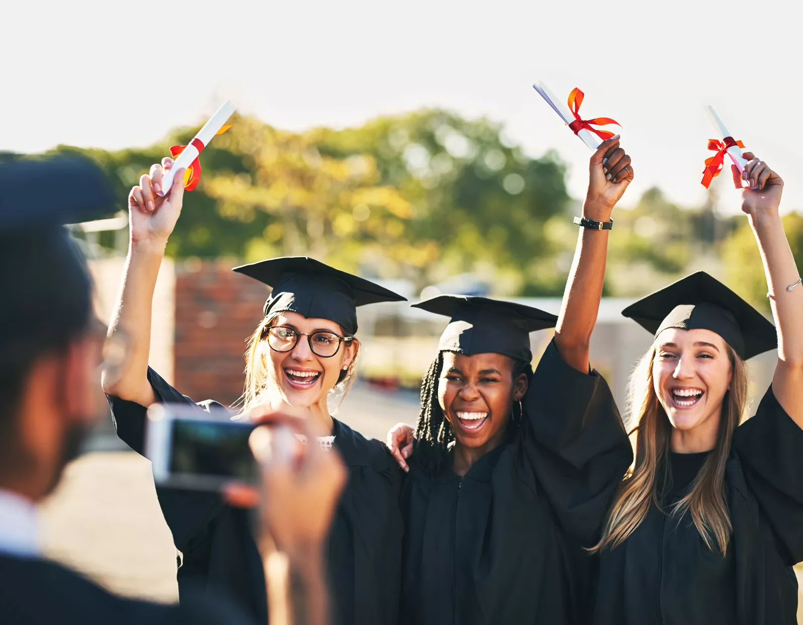 three graduates smiling and posing for camera while holding their diplomas in the air